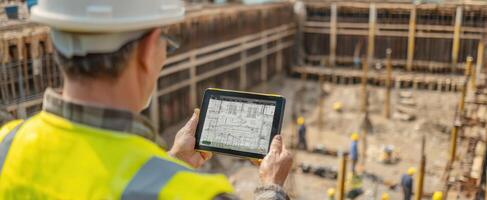 The construction worker analyzing plans on a tablet at the building site. photo