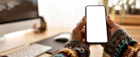 The smartphone held in hands showcasing a blank screen in a cozy workspace. photo