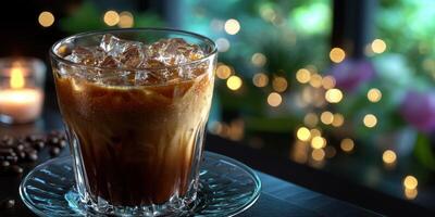 Cold beverage served on a table with ice cubes, candlelight, and a blurred garden view in the background during evening time photo