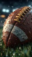 Rain-soaked football resting on wet grass in a stadium during a night game photo