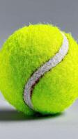 Bright green tennis ball resting on a smooth surface showcasing its fuzzy texture and distinct white line photo