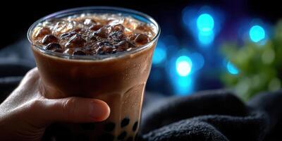 Freshly prepared bubble tea with ice in hand during evening gathering with glowing background photo