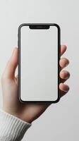 Hand holding a smartphone with a blank screen against a neutral background in a modern setting photo