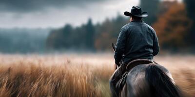Cowboy riding a horse through tall grass in a misty landscape during early morning light photo