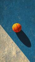 Bright orange basketball resting on the blue and white textured court during sunny daylight hours photo