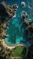 Stunning aerial view of a beachside soccer field surrounded by clear turquoise water and rocky coastal formations photo