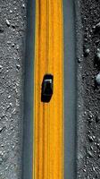 Black car driving on a winding yellow road surrounded by rocky terrain in a remote area during daytime photo