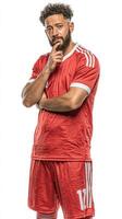 Professional soccer player in red uniform posing thoughtfully in studio setting during daytime photo