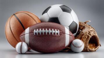 Various sports balls displayed together with a baseball glove on a neutral background showcasing athletic equipment diversity photo