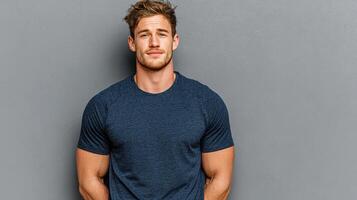Young man in casual attire poses confidently against a gray wall, showcasing a relaxed yet stylish demeanor in a modern setting photo