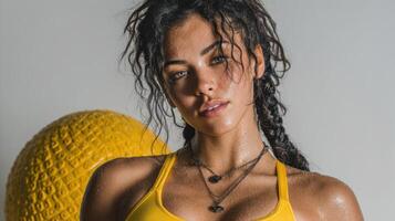 Young woman in yellow sportswear poses confidently with textured exercise ball indoors after workout session photo