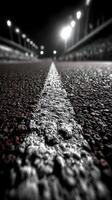 Empty racetrack at night with bright lights illuminating the surroundings and a focus on the textured asphalt surface photo
