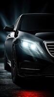 Luxury black sedan with glowing headlights parked in a dimly lit urban environment at night photo