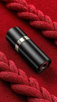 Elegant black cylindrical object placed on a vibrant red textured surface alongside intertwined red fibers photo