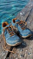 Wet blue sneakers resting on a wooden dock beside clear water during a sunny day in a serene outdoor setting photo