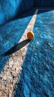 Vibrant orange ball resting on textured blue surface with contrasting white line during afternoon light photo