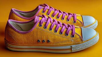 Bright yellow sneakers with pink laces displayed against a vibrant orange background photo
