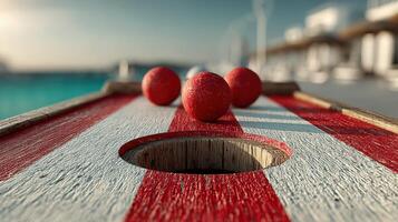 Colorful balls roll toward a hole on a red and white striped game board near the water at sunset photo