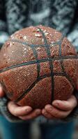 Old basketball held by hands in a cozy sweater, showcasing wear and texture on a chilly day outdoors photo