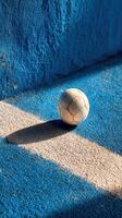 Soccer ball rests on textured blue and gray surface during bright daylight photo