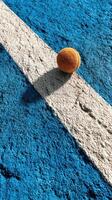 Tennis ball rests on the blue court surface near the white line during a sunny afternoon photo