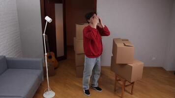 Stressed young man covering face with hands surrounded by moving boxes in new apartment video