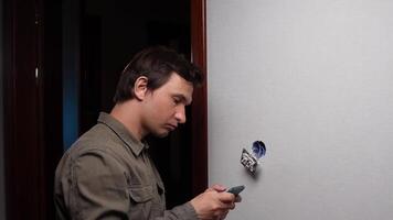 Electrician installing light switch and consulting instructions on smartphone video