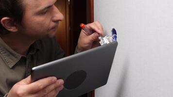 Electrician installing light switch and consulting tablet video