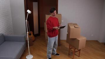 Mens gebruik makend van tablet en organiserende dozen in nieuw appartement na in beweging in video