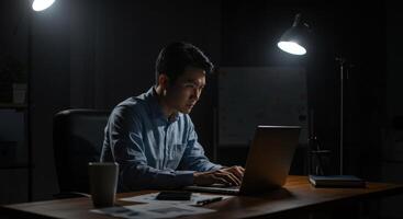 Asian man working on laptop late at night photo
