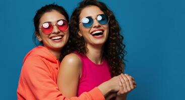 Two happy young women friends hugging and laughing wearing colorful sunglasses photo