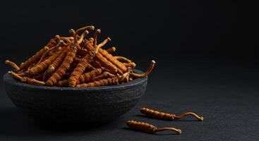 Dried Cordyceps Sinensis Mushrooms in a Dark Stone Bowl with Pieces on Black Surface photo