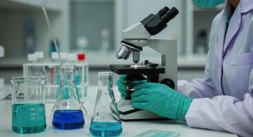 Laboratory technician examining sample under microscope in science lab with beakers photo
