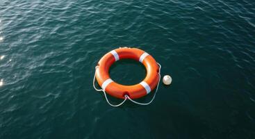 Orange lifebuoy with white bands floating on calm dark water surface photo