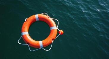 Bright orange lifebuoy with white stripes floating on calm dark water photo