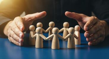 Hands shielding a circle of wooden figures holding hands on a blue surface photo