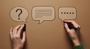 Hands drawing communication symbols speech bubbles question text dots on brown paper photo