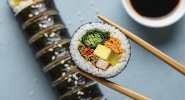 Closeup of kimbap slice held by chopsticks with rolls and soy sauce photo