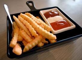 French fries or fried potato put on a black square ceramic plate accompanied by set of tomato sauce, chili sauce and mayonnaise. photo
