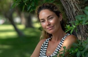 Woman enjoys warm summer day leaning against oak tree in striped tank top amidst green foliage photo