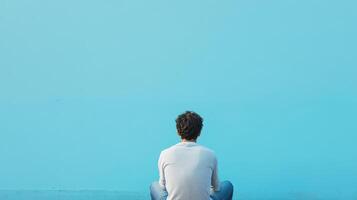 Person sitting alone against a blue wall photo