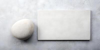 Minimalist Composition of a Smooth Pebble Next to a Blank White Rectangle on a Textured Gray Surface for Creative Design Use photo