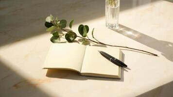 Blank notebook with pen and eucalyptus branch on a brightly lit surface for creative writing photo