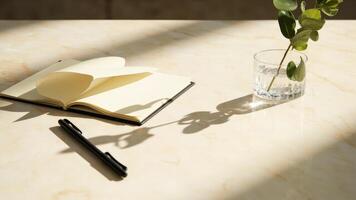 Aesthetic workspace with a notebook pen and vase of greenery on a marble surface photo