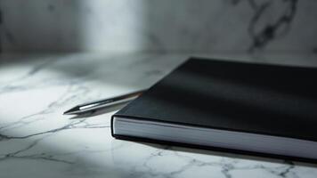 Minimalist black notebook and pen resting on a marble surface in natural light photo
