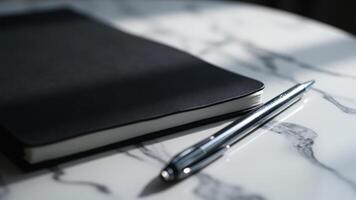 Minimalist composition of black notebook and silver pen resting on a marble tabletop photo