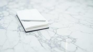 Minimalist composition featuring a blank white notebook and pen resting on a marble surface photo