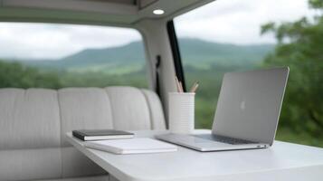 Mobile Office in a Van. A portable workspace with a laptop, notebooks, and pencils set up on a fold out table inside a van, overlooking a scenic landscape photo