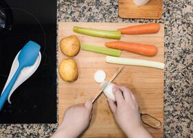 High angle of view of woman hands chopping a turnip against a wood cutting board at home kitchen. photo