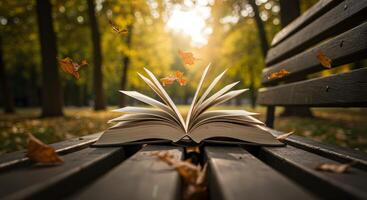 An open book is sitting on a bench in the park with autumn leaves flying around it photo
